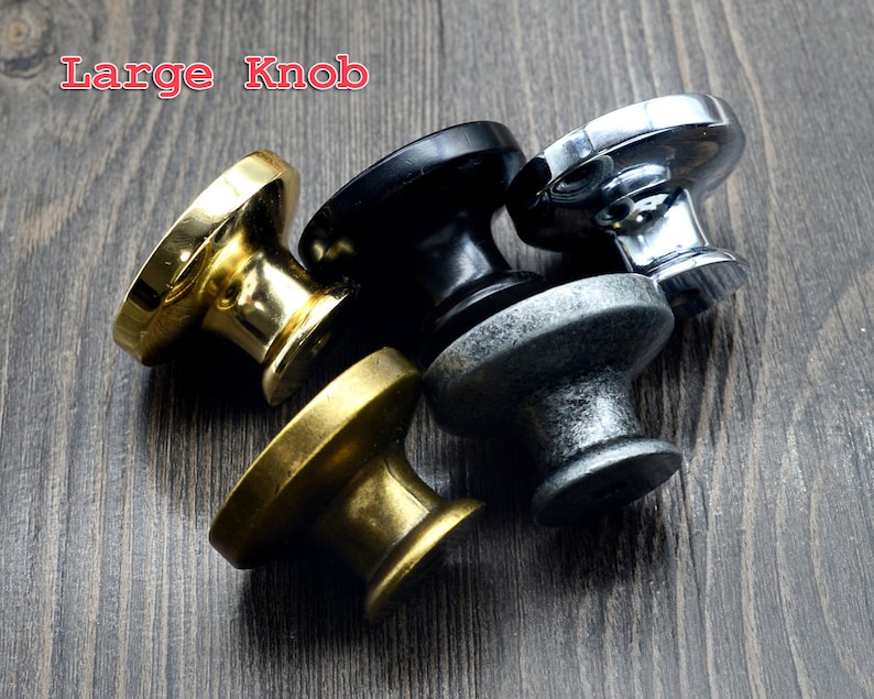Pode incluir: Quatro bot&otilde;es de arm&aacute;rio em diferentes acabamentos: lat&atilde;o polido, preto, prata e estanho envelhecido. Os bot&otilde;es s&atilde;o redondos com um centro elevado e uma superf&iacute;cie lisa. O texto "Large Knob" &eacute; vis&iacute;vel no canto superior esquerdo da imagem.