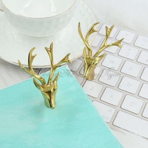 Puede incluir: Dos esculturas de cabeza de ciervo doradas con cuernos. Las esculturas están sobre una superficie turquesa y un teclado blanco.