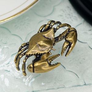 Puede incluir: Un tirador de caj&oacute;n de lat&oacute;n en forma de cangrejo con un dise&ntilde;o detallado. El tirador es un acento decorativo para muebles.