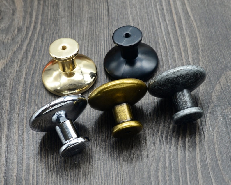 Pode incluir: Quatro bot&otilde;es de arm&aacute;rio diferentes em v&aacute;rios acabamentos: dourado, prateado, preto e cinza. Os bot&otilde;es s&atilde;o todos redondos e t&ecirc;m um design simples.