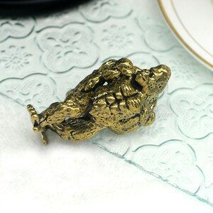 K&ouml;nnte beinhalten: Eine goldfarbene Metallfigur aus zwei ineinander verschlungenen Figuren, die m&ouml;glicherweise ein Paar oder eine mythische Kreatur darstellen. Die Figur ist mit strukturierten Oberfl&auml;chen und filigranen Designs verziert.