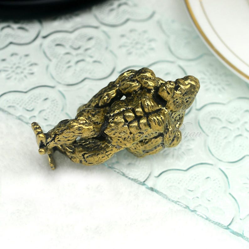 K&ouml;nnte beinhalten: Eine goldfarbene Metallfigur aus zwei ineinander verschlungenen Figuren, die m&ouml;glicherweise ein Paar oder eine mythische Kreatur darstellen. Die Figur ist mit strukturierten Oberfl&auml;chen und filigranen Designs verziert.