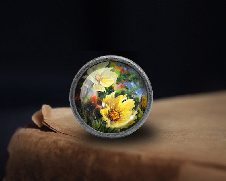 May include: A silver knob with a round glass top featuring a painted image of yellow flowers with a blue and green background.