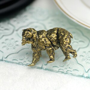 May include: A gold-toned metal bear figurine with a detailed, textured surface. The bear is walking with its head turned to the side.