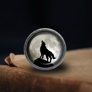 May include: A silver-toned round knob with a glass insert featuring a black silhouette of a wolf howling at the moon.