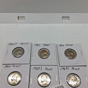 May include: A collection of six proof nickel coins in protective sleeves. The coins are dated 1960, 1962, 1964, 1964, 1968, and 1969. Each coin features a profile of a man on the obverse.