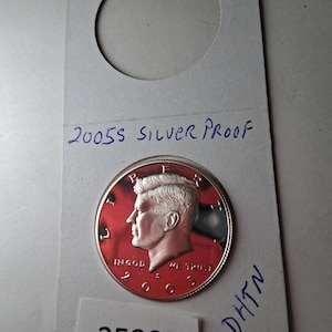 May include: A silver 2005S Kennedy half dollar proof coin. The coin is in a protective holder with the text "2005S SILVER PROOF" and the number "25985". The coin features a profile of John F. Kennedy.