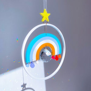 May include: A rainbow-coloured wooden mobile with a crystal prism hanging in the centre. The mobile is suspended from a white ceiling and has a yellow star at the top.