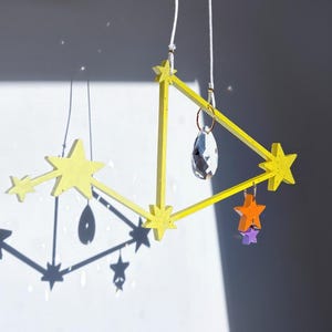 May include: A yellow wooden mobile with stars and a crystal hanging from it. The mobile is suspended from the ceiling.