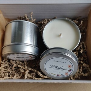 May include: Two round silver metal candle tins with white wax and cotton wicks. One tin is closed with a label reading Littledrops Lavender, while the other is open. The second tin has a label reading Littledrops Lime Basil Mandarin.