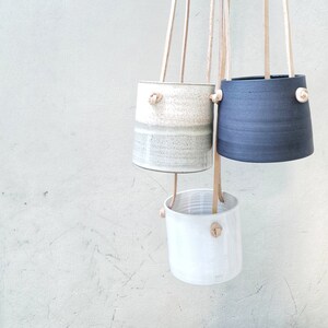 May include: Three hanging ceramic planters with leather straps. The planters are in shades of white, gray, and black.