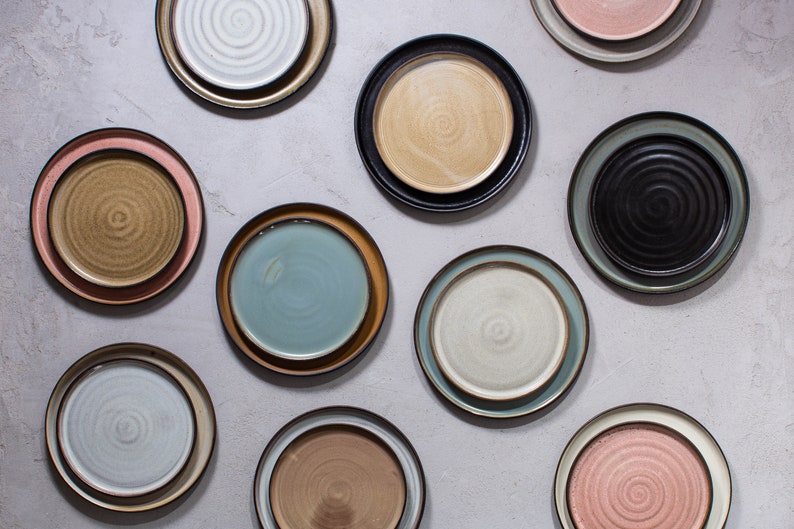 Pode incluir: Uma cole&ccedil;&atilde;o de dez pratos de cer&acirc;mica em v&aacute;rias cores e padr&otilde;es, incluindo azul, verde, marrom e rosa. Os pratos est&atilde;o dispostos em um padr&atilde;o de grade sobre um fundo cinza claro.