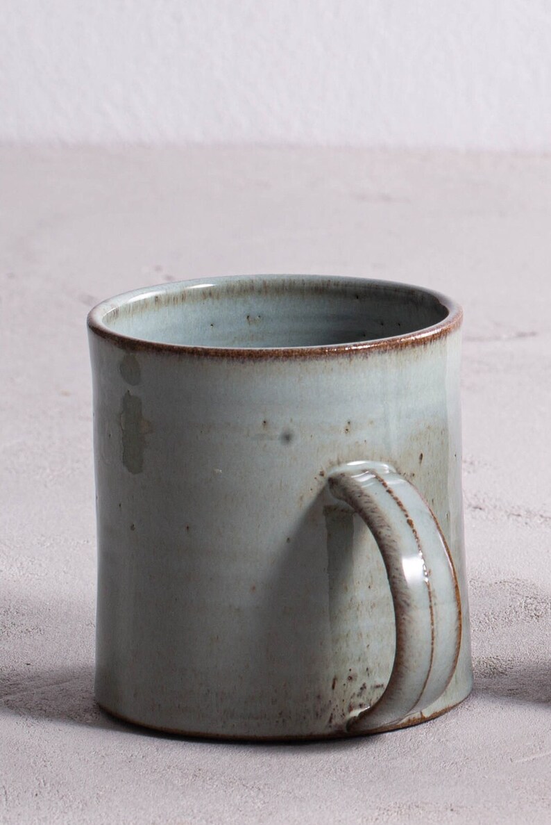 Pu&ograve; includere: Una tazza in ceramica blu chiaro con un bordo marrone e un manico. La tazza ha una glassa macchiata e un aspetto rustico.