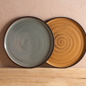 May include: Two ceramic plates with a swirl design. The plate on the left is a light blue color with a dark brown rim. The plate on the right is a light brown color with a dark brown rim.