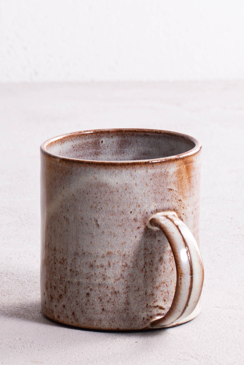 Pu&ograve; includere: Una tazza in ceramica marrone e bianca con una glassa macchiata. La tazza ha un manico arrotondato.
