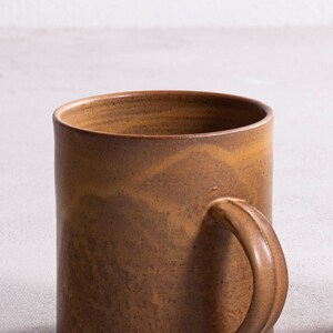Pu&ograve; includere: Una tazza in ceramica marrone con un manico arrotondato. La tazza ha una smaltatura macchiata e screziata.