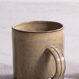 Pu&ograve; includere: Una tazza in ceramica di colore marrone chiaro con una glassa macchiata e un manico arrotondato.