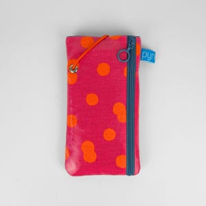 Può includere: Una custodia per telefono in tessuto rosa con pois arancioni. La custodia ha una cerniera blu e un'etichetta blu con la scritta "pyn". Un cordino elastico arancione è attaccato in alto.