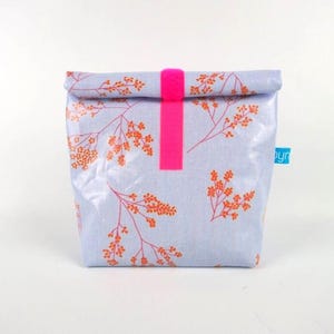 Op de afbeelding: Een lichtblauwe lunchtas met een oranje en roze bloemenpatroon. De tas heeft een felroze bandsluiting. Een klein blauw label is aan de zijkant bevestigd. De tas is gemaakt van duurzaam, waterdicht materiaal.