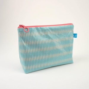 Pode incluir: Uma bolsa de zíper azul claro e branco com um padrão, um zíper rosa e uma etiqueta azul que diz "lyr".