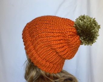 May include: A bright orange knitted beanie with a green pom-pom on top.