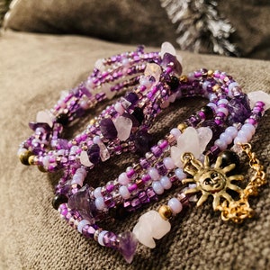 Puede incluir: Pulsera envolvente de m&uacute;ltiples hilos con piedras de amatista y cuarzo, cuentas de semillas y un dije de sol dorado. La pulsera es principalmente morada con acentos blancos y dorados. La pulsera mide unos 18 cm de largo.