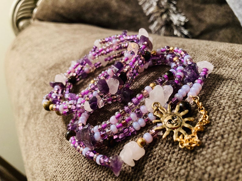 Puede incluir: Pulsera envolvente de m&uacute;ltiples hilos con piedras de amatista y cuarzo, cuentas de semillas y un dije de sol dorado. La pulsera es principalmente morada con acentos blancos y dorados. La pulsera mide unos 18 cm de largo.
