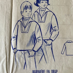 Könnte beinhalten: Ein Vintage-Schnittmuster für ein Matrosenhemd in Blau auf braunem Hintergrund. Das Schnittmuster ist für Kinder im Alter von 8 und 10 Jahren. Der Text auf dem Schnittmuster lautet "Marinière en drap pour enfants de 8 et 10 ans Patron du mois N° 2599 Juillet 1967".