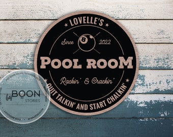 May include: A black and brown wooden sign with the text "* LOVELLE'S * Since 2022 POOL ROOM Rackin' & Crackin' QUIT TALKIN' AND START CHALKIN'" and a graphic of a pool ball with crossed cues.
