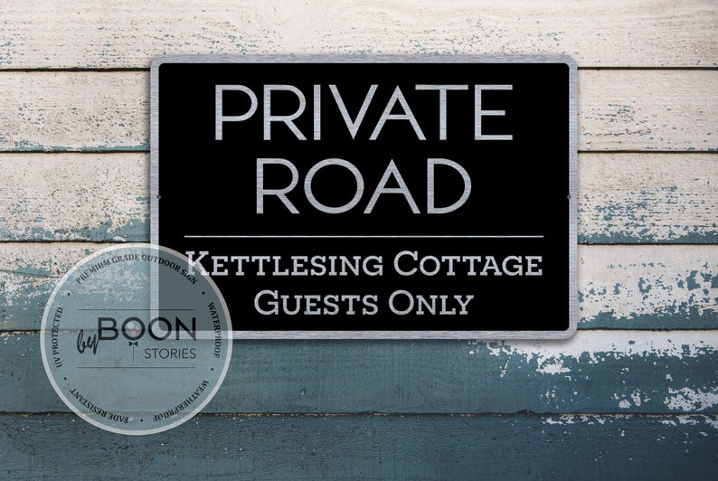 May include: A black and silver metal sign with the text "PRIVATE ROAD" and "KETTLESING COTTAGE GUESTS ONLY".