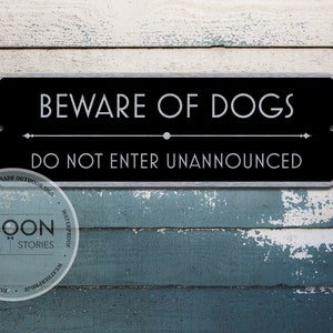 May include: A black and silver metal sign with the text "Beware of Dogs. Do Not Enter Unannounced." The sign is mounted on a weathered blue wooden surface.