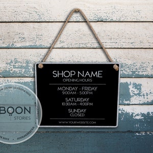 Pode incluir: Placa preta com texto branco pendurada em um fundo de madeira azul e branco desbotado. A placa diz "SHOP NAME" e lista as horas de abertura da loja. A placa também inclui o endereço do site "WWW.YOURWEBSITE.COM".