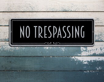 Pode incluir: Uma placa preta e prateada com o texto "NO TRESPASSING" em letras brancas sobre um fundo de madeira envelhecido.