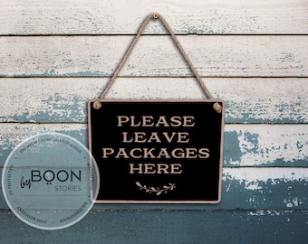May include: A rectangular black sign with the text "PLEASE LEAVE PACKAGES HERE" in a serif font. The sign is framed in a copper color and hangs from a jute rope against a weathered, painted wood background.