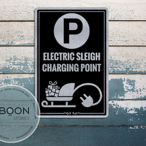 Puede incluir: Un letrero de metal negro y plateado con el texto "Punto de carga para trineo eléctrico" y un símbolo de estacionamiento. El letrero también presenta una imagen de dibujos animados de un trineo con regalos y un enchufe.