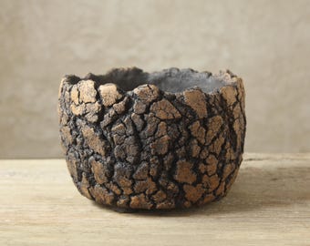 May include: A round, bowl-shaped planter featuring a highly textured, cracked exterior surface. The finish displays a deep, dark brown base color with metallic bronze highlights on the raised, uneven edges of the cracked, rock-like pattern.