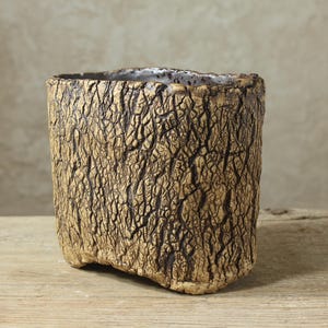 May include: A ceramic planter with a textured exterior that mimics the appearance of tree bark. The surface features a metallic gold finish with dark brown crevices, and the interior is glazed in a smooth, glossy white finish.