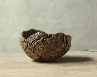 Puede incluir: Un cuenco artesanal texturizado con una estética natural y terrosa. El cuenco es de color marrón cálido, con una textura rugosa y orgánica que recuerda a la corteza de un árbol. Se encuentra sobre una superficie de madera, mostrando su diseño rústico único.