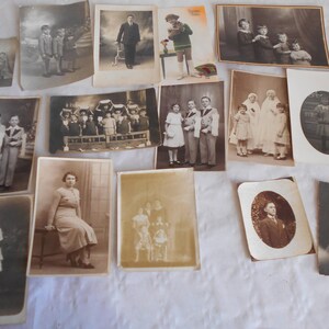 May include: A collection of vintage black and white photographs in various sizes and frames. The photos depict people in different settings, including a group of children, a family portrait, and a single person.