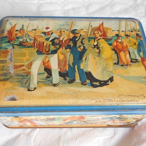 Può includere: Scatola di latta rettangolare con una scena dipinta di persone vicino a un porto. La scatola ha un bordo blu e la scena raffigura figure in abiti tradizionali, barche e il testo "SUR LE PORT A CONCARNEAU".