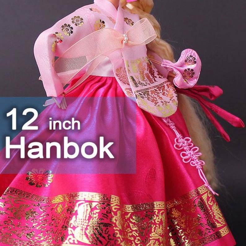 Puede incluir: Vestido de mu&ntilde;eca Hanbok de 30 cm en tonos rosa y rojo, con detalles dorados. La prenda tradicional coreana presenta intrincados estampados florales y un lazo decorativo. El texto "12 inch Hanbok" aparece en la imagen.