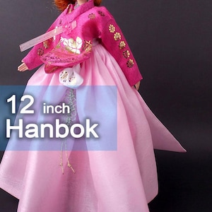 Pode incluir: Boneca Hanbok de 30 cm com uma roupa tradicional coreana. A roupa da boneca &eacute; rosa vibrante com bordados florais dourados nas mangas e no corpete. A saia &eacute; de um tom rosa mais claro.