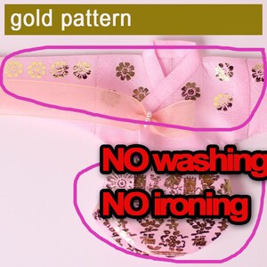 Puede incluir: Prenda rosa con detalles florales dorados. Incluye un lazo con una perla. El texto "NO washing" y "NO ironing" es visible.