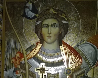 May include: A Byzantine-style icon depicting a female saint, possibly Saint Barbara, in a golden halo. She is wearing a crown, armor, and a red and gold robe. She holds a cross in her right hand and a bow and arrow in her left hand. The icon is painted on a wooden panel and has a gold background.