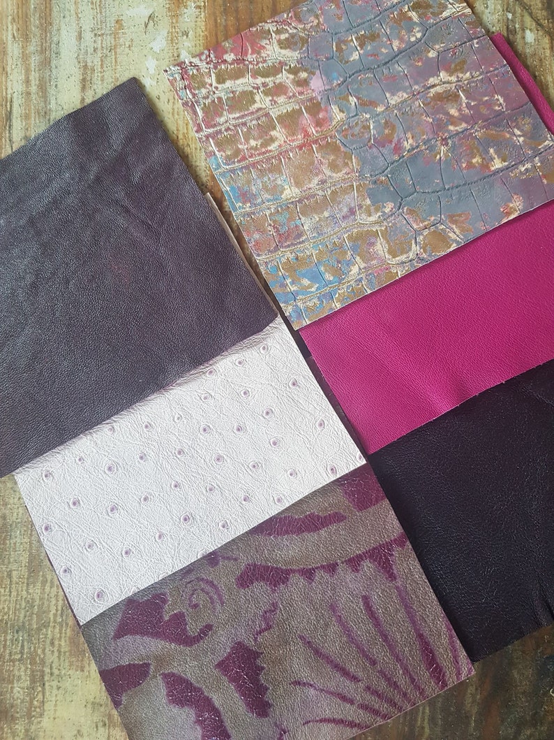 May include: A collection of six different leather swatches in various colors and textures, including a dark purple, white with small dots, a purple and brown patterned leather, a dark purple, a bright pink, and a light blue and brown patterned leather.
