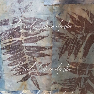 May include: A close-up of a fabric art piece with a blue and brown color scheme. The fabric is textured and has a pattern of leaves. The artist's name, "Beata Jarmolowska", is written in white cursive on the fabric.