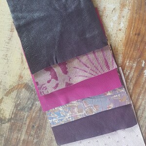 May include: A stack of six different leather swatches in various shades of purple, pink, and gray. The swatches are arranged in a vertical stack, with the darkest shade at the top and the lightest shade at the bottom.