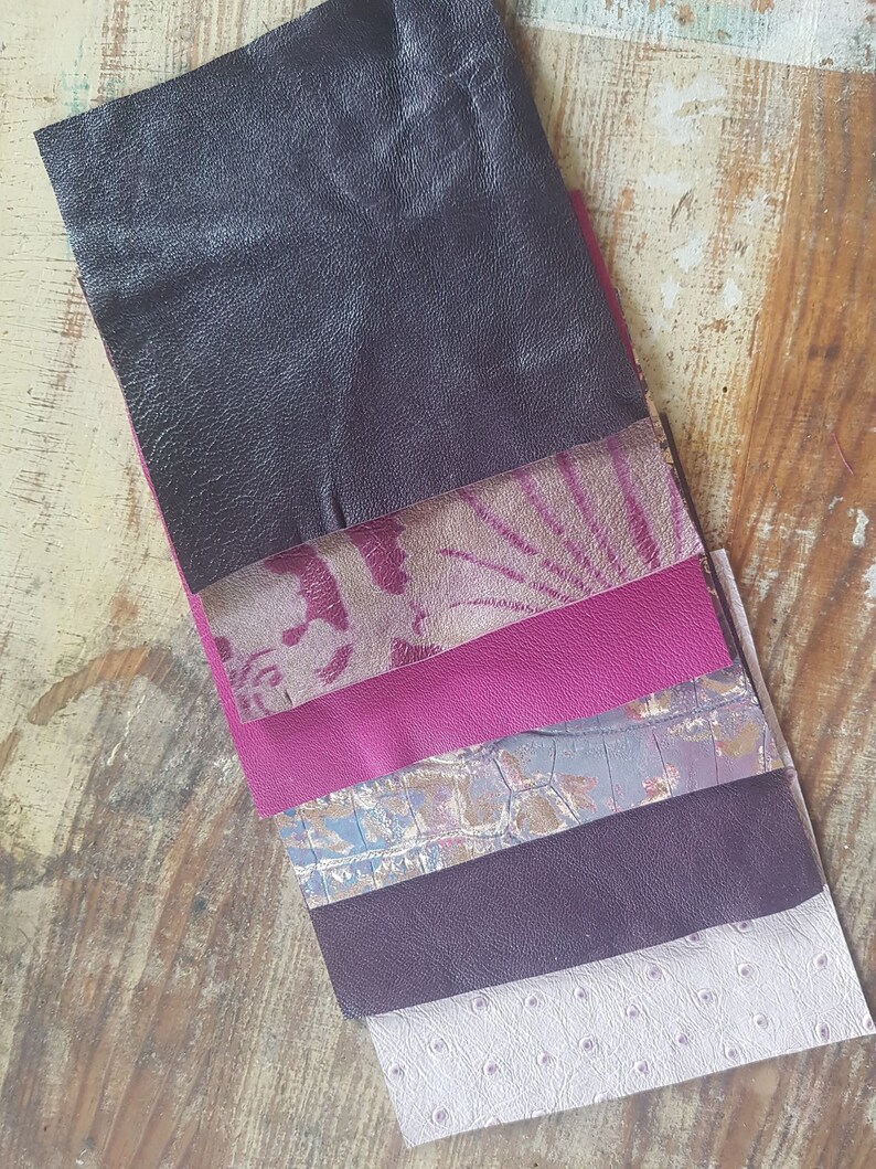 May include: A stack of six different leather swatches in various shades of purple, pink, and gray. The swatches are arranged in a vertical stack, with the darkest shade at the top and the lightest shade at the bottom.