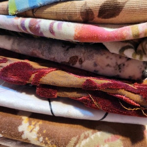 Può includere: Un mucchio di ritagli di tessuto in vari colori e motivi, tra cui disegni floreali, paisley e geometrici. I tessuti sono un mix di texture, tra cui velluto, velluto a coste e cotone.