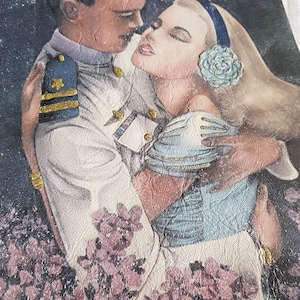 以下が含まれることがあります： 星が散りばめられた暗い青色の背景に、抱き合うカップルが描かれたヴィンテージの革ジャン。男性は金色のアクセントがついた白い制服を着ており、女性は白い花を髪につけた青いドレスを着ています。